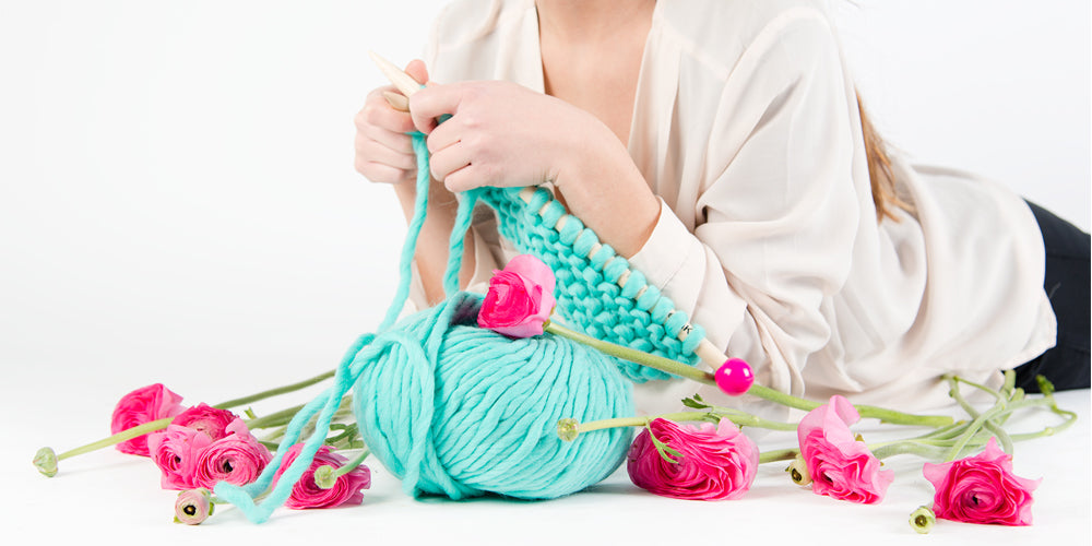 Woman Knitting with Chunky Wool Yarn and Wooden Needles Surrounded by Pink Flowers
